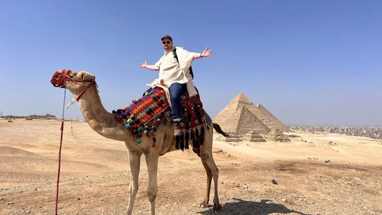 Jonas on a camel with arms wide open in front of the Giza pyramids, Egypt